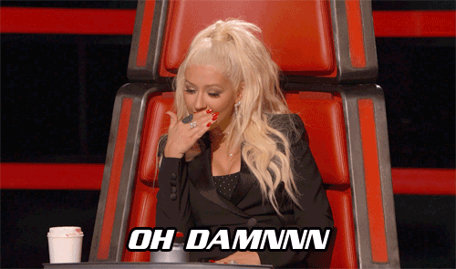 Photo of Christina Aguilera with her hand over her mouth sitting in judge chair on The Voice with text overlay "OH DAMNNN"