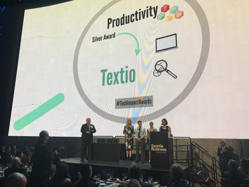 Photo of Kieran Synder and Textio employees accepting award at Tech Impact Awards Gala with banner in background that reads "Productivity Silver Award Textio"
