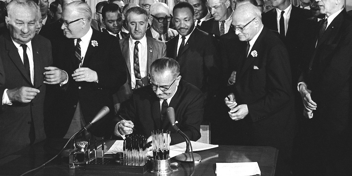 Dr. Martin Luther King looks on as President Lyndon Johnson signs the Civil Rights Act of 1964