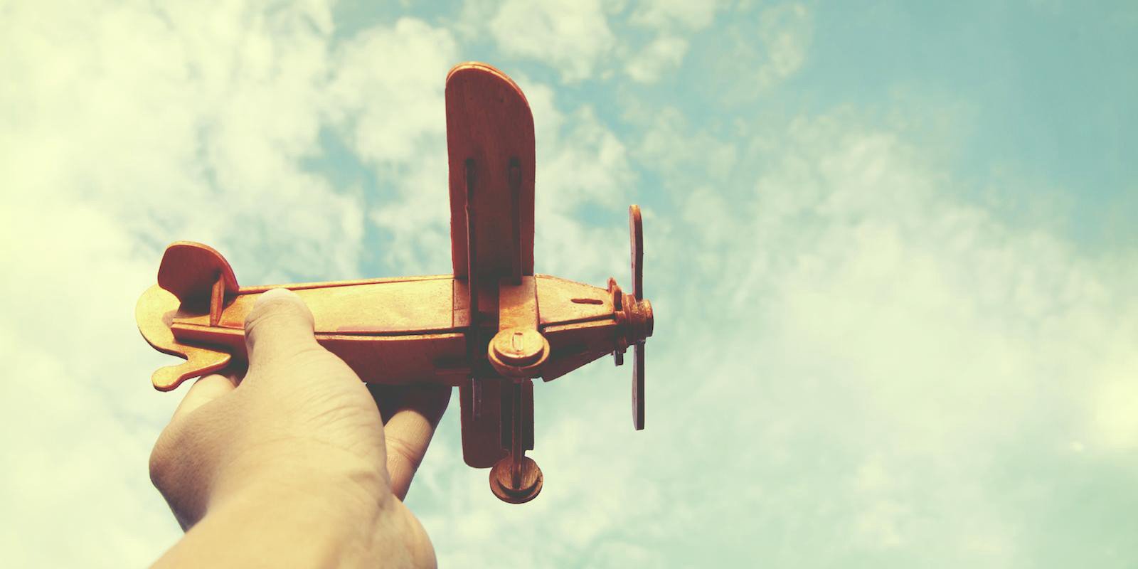 Person's hand flying a wooden prop plane against a lightly cloudy blue sky
