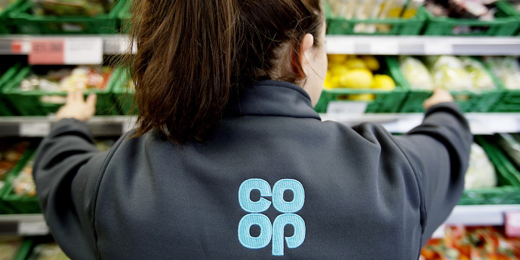 Image of a person wearing an embroidered co-op jacket in a produce isle, Photo by The Co-Op Group